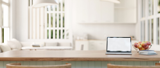 A laptop mockup on a wood kitchen island in a modern white home studio with living room and kitchen. - obrazy, fototapety, plakaty