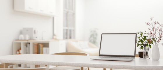 A white-screen laptop mockup on a dining table in a modern white living room. close-up image