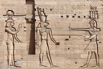 Ancient Egyptian bas-relief on stone wall with figures of the goddess Isis, the god Horus and...