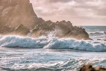 Fototapeta premium Wave splashes close-up. Crystal clear sea water hitting rock formations in the ocean in San Francisco Bay, blue water, pastel colors.