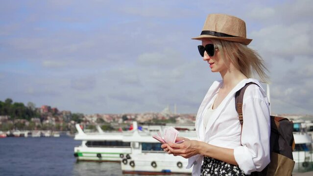 Traveler girl with backpack and saloon hat on background of pier with ships counts banknotes of Turkish lira. Hands holding two hundred lira Turkish lira banknotes. Travel Leisure.