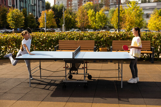Young teenager girl playing ping pong. She holds a ball and a racket in her hands. Playing table tennis outdoors in the yard - Powered by Adobe