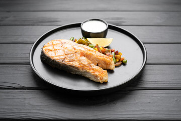 Grilled salmon steak with vegetables mix on black background, top view.