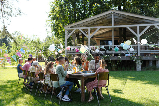 Family and friends sitting at the party table during a summer garden party outdoors. Decorations and beautiful wooden gazebo at background.