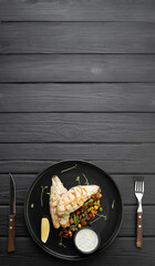 Grilled BBQ fish fillet with cooked vegetables on dark background, top view