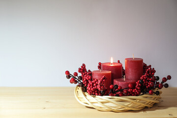 First advent with four red candles, one of them lighted, in a natural willow wicker wreath with berry decoration, seasonal home decor, copy space, selected focus - obrazy, fototapety, plakaty