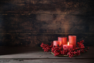 Frist Advent with red berry decoration and candles in a wreath, one is lighted, holiday home decor against a dark rustic wooden background, copy space, selected focus - 666938872