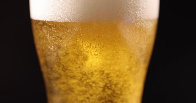 Golden beer pouring into glass with foam and many gas bubbles closeup 4k movie slow motion. Alcohol addiction concept