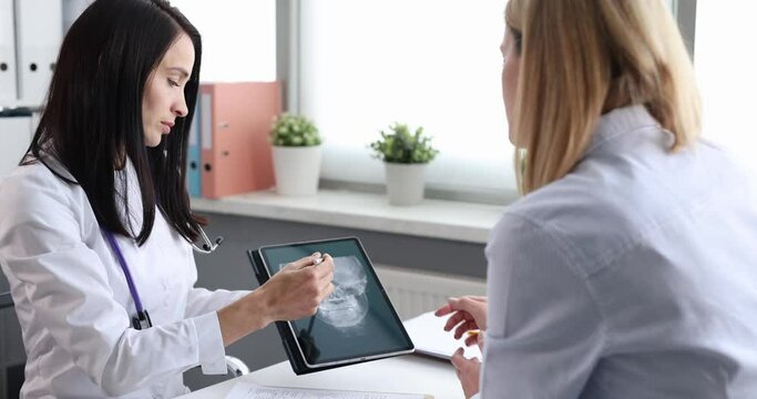 Doctor otorhinolaryngologist showing woman patient digital tablet with xray of sinuses 4k movie slow motion. Diagnosis and treatment of acute sinusitis concept