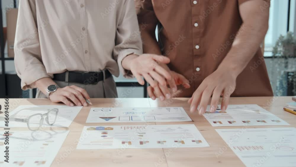 Poster midsection shot of two unrecognizable office employees standing near desks and brainstorming ideas a