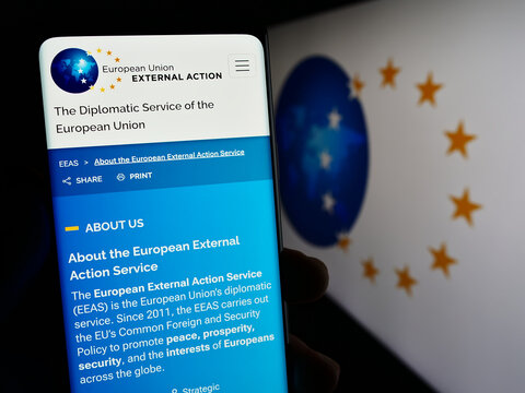 Stuttgart, Germany - 10-16-2023: Person holding cellphone with webpage of EU institution European External Action Service (EEAS) with logo. Focus on center of phone display.