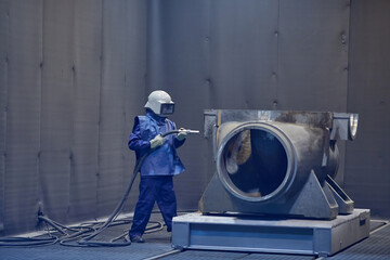 worker processes workpiece with sandblasting tool in factory, selective focus
