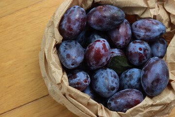 Close-up of purple plums in a brown paper bag on wooden table with selective focus