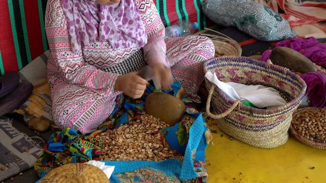 Woman working in a cooperative to manufacture argan fruits, using small stones to crack the fruit open to find the argan nut, extracting the kernels.