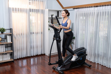Fototapeta na wymiar Energetic and strong athletic asian woman running on elliptical running machine at home. Pursuit of fit physique and commitment to healthy lifestyle with home workout and training. Vigorous