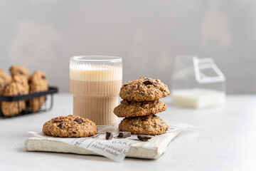 Homemade oatmeal cookies with banana, oats, nuts and chocolate drops on a wooden board with a glass of latte on light background. Side view, copy space for text. Healthy food. Oatmeat biscuits.