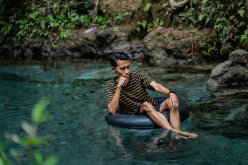 A man enjoys a very clean spring river using a float tube. Located on the Udal Gumuk river, Magelang, Central Java, Indonesia.