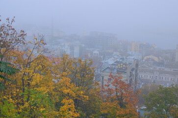 Aerial foggy landscape view of ancient Podil neighborhood. Mysterious cityscape. Kyiv in autumn thick fog. Tree leaves boarder