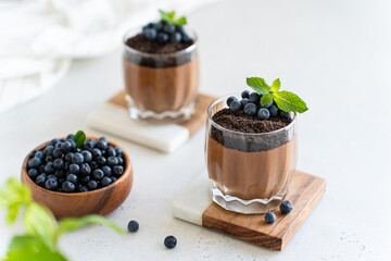 Vegan chocolate mousse in glasses decorated with fresh blueberry and mint on a marble board on white concrete background. Close up. Protein diet recipe. Creamy chocolate yogurt, panna cotta dessert