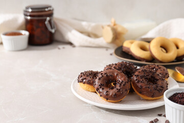 Fototapeta na wymiar Chocolate donuts on plates, bowls, milk bottle and jar on light background, space for text