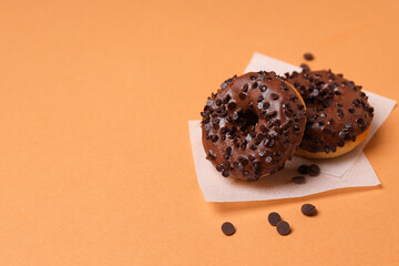 Chocolate donuts on paper on orange background, space for text