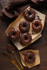 Chocolate donuts on paper, towel and cutlery on wooden background, top view
