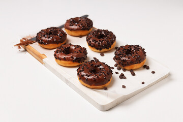 Chocolate donuts on kitchen board and knife on white background