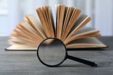 Magnifier and open book on wooden table on light background