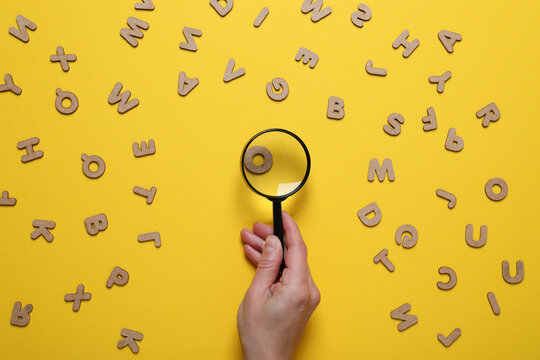 Magnifier in hand and letters on yellow background, top view