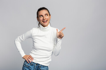 Portrait of an attractive woman pointing at blank space, white top, business style, on light grey studio background