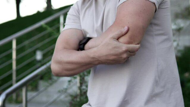A man feels acute pain in his elbow joint while walking in the evening. Sports and injury concept.