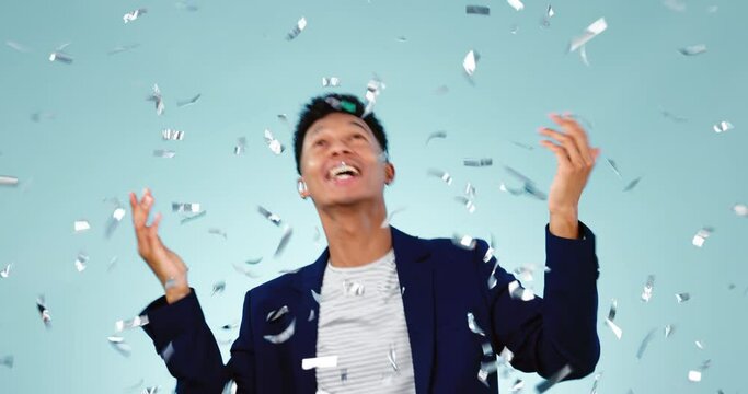 Confetti, dance and celebration of excited man in studio isolated on a blue background. Glitter, happy and person at party moving with energy for success, achievement of goal and winner of lottery