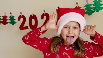 Funny excited happy toddler girl wearing Christmas costume red Santa hat decorates winter holiday house for New Year party of handmade paper garland numbers 2024. crafts for kids DIY. home decoration