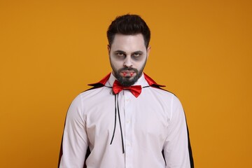 Man in scary vampire costume with fangs on orange background. Halloween celebration