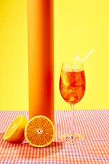 Glass of delicious, refreshing Aperol spritz cocktail with oranges standing on checkered tablecloth over yellow background. Concept of alcohol drinks, party, holidays, bar. Poster. Copy space for ad