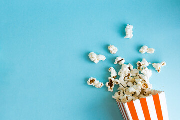 Red and white stripped popcorn box with a popcorn around on a blue background. TV watching concept...