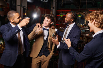 Fototapeta na wymiar happy interracial groomsmen in formal wear congratulating friend in bar, men with glasses of whiskey