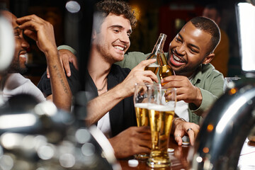 three interracial friends toasting with glasses of beer while spending time in bar, male friendship