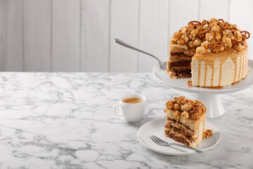 Caramel drip cake decorated with popcorn and pretzels served on white marble table, space for text