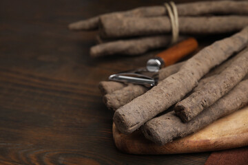 Raw salsify roots and peeler on wooden table, closeup. Space for text