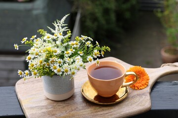 Cup of delicious chamomile tea and fresh flowers outdoors