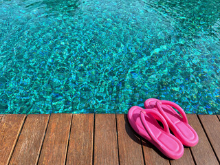 Clear rippled water in swimming pool and pink flip-flops on wooden deck outdoors. Space for text