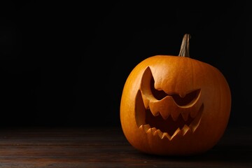 Scary jack o'lantern made of pumpkin on wooden table in darkness, space for text. Halloween traditional decor