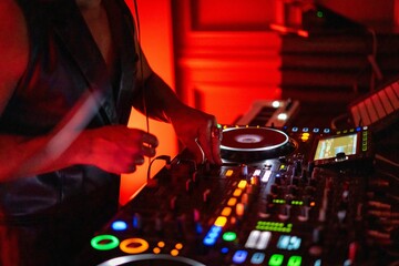 DJ working on a professional controller in a dimly lit room, with illuminated buttons