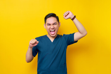 Excited professional young Asian male doctor or nurse wearing a blue uniform standing confidently...