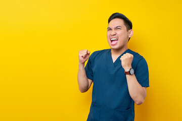 Excited professional young Asian male doctor or nurse wearing a blue uniform standing confidently...