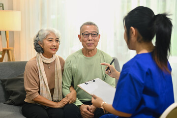 Obraz premium Smiling senior couple listening attentively to nurse or general practitioner explaining therapy details during home visit