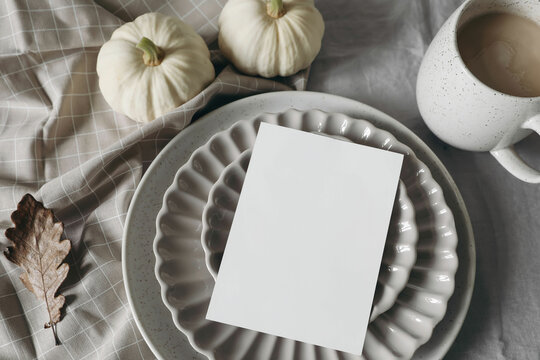 Neutral autumn stationery. Fall mockup scene with blank greeting card, invitation, craft envelope. White pumpkins. Scalloped plate, cup of coffee. Linen table cloth, oak leaves. Flatlay. Thanksgiving.