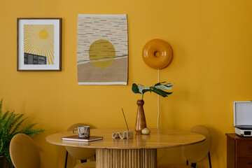 Warm and cozy composition of dinning room interior with mock up poster frame, kilim rug, round table, yellow chair, wall, vase with leaves, books and personal accessories. Home decor. Template.