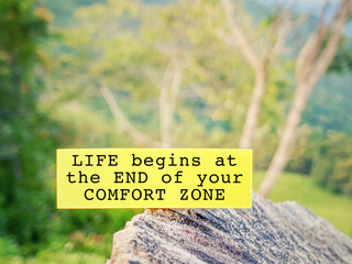 Inspirational motivating quote - life begins at the end of your comfort zone on paper with blurred nature background.
